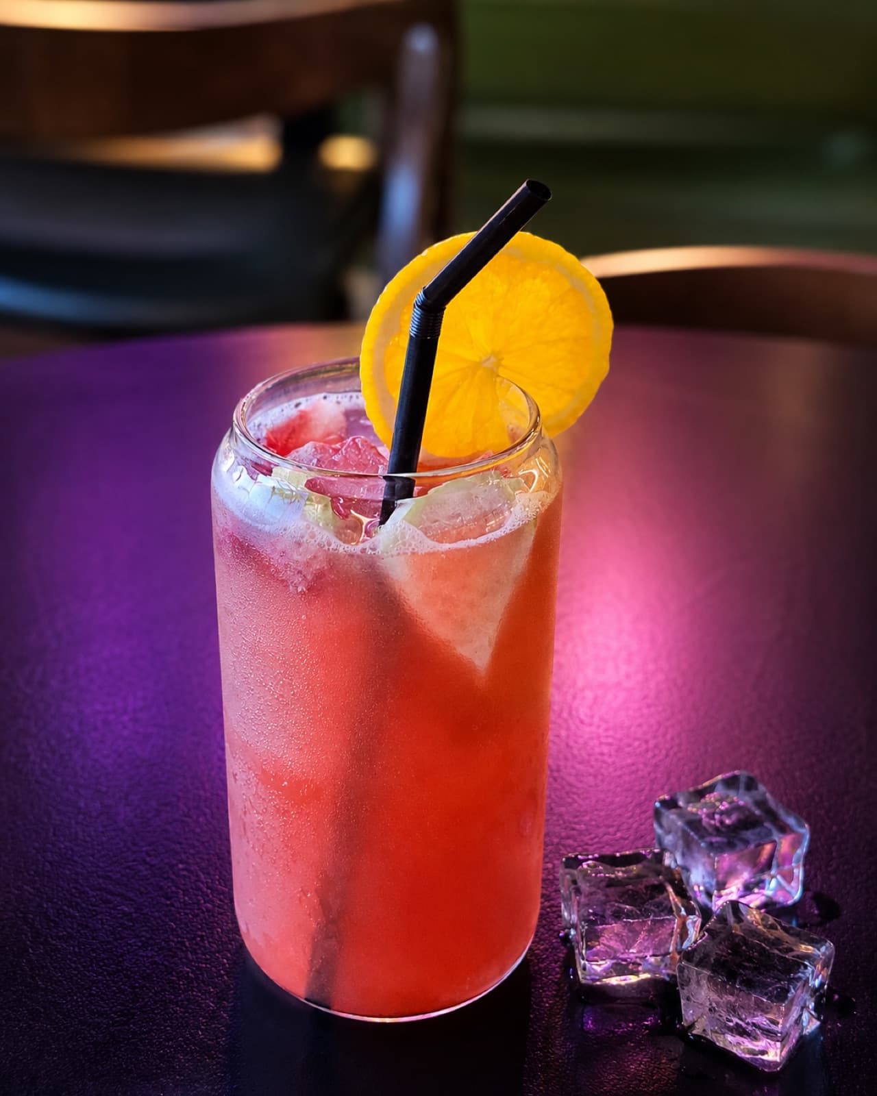Iced fruit drink with an orange slice under neon lighting